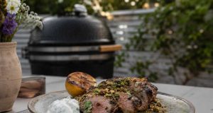 Grillad lammytterfilé med pistage, mynta och grillad citron Sliced herb-crusted grilled beef on a plate with a lemon half, white sauce dollop, and pistachio crumble, outdoors near a grill.