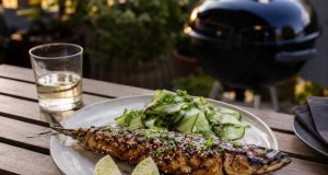 Grilled whole fish with sesame and herbs on a plate, lime wedges and cucumber salad on the side.