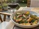 Bowl of roasted potato wedges with dill on a wooden outdoor table, barbecue in the background