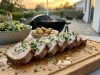 Fläskytterfile med Vitlökssmör och Örter Herb-garnished sliced pork tenderloin on a wooden board, with a side salad and roasted potatoes, outdoor sunset patio.
