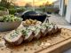 Herb-garnished sliced pork tenderloin on a wooden board, with a side salad and roasted potatoes, outdoor sunset patio.