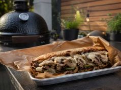 Loaded steak sandwich with onions, peppers and melted cheese on a toasted roll, served on parchment.