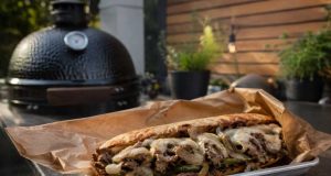 Loaded steak sandwich with onions, peppers and melted cheese on a toasted roll, served on parchment.