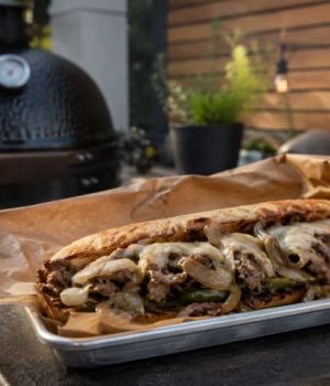 Loaded steak sandwich with onions, peppers and melted cheese on a toasted roll, served on parchment.