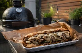 Loaded steak sandwich with onions, peppers and melted cheese on a toasted roll, served on parchment.