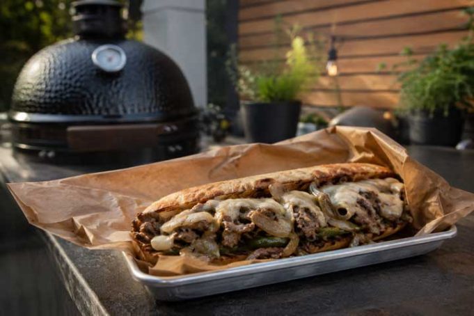 Loaded steak sandwich with onions, peppers and melted cheese on a toasted roll, served on parchment.