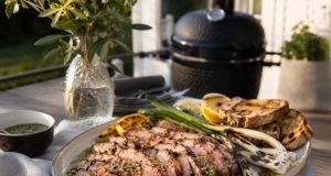 Pluma på grillen med sherryvinägrett och sotad salladslök Sliced medium-rare steak on a platter with lemon wedges, grilled bread, and asparagus, outdoors near a barbecue grill.