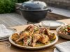 Herb-roasted whole chicken on a platter with lemon wedges on an outdoor wooden table.