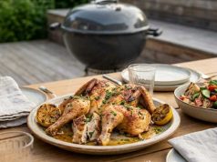 Spatchcock-kyckling på grillen med vitlökssmör, örter och grillad citron Herb-roasted whole chicken on a platter with lemon wedges on an outdoor wooden table.