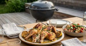 Herb-roasted whole chicken on a platter with lemon wedges on an outdoor wooden table.