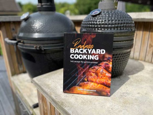 Recension: Bad Ass Backyard Cooking av Johan “Big Swede” Magnusson Paperback cookbook titled 'Badass Backyard Cooking' rests on a concrete railing with two smokers in the background.